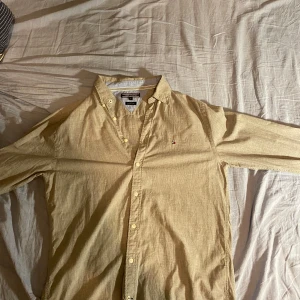 Beige skjorta från Tommy Hilfiger - Snygg beige skjorta från Tommy Hilfiger i storlek M. Skjortan har en klassisk krage och knappar framtill. Perfekt för en stilren look. 2an bild kan man se två fläkar om man kollar riktigt noga men inget man märker med blotta ögat. Skick 9/10