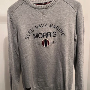 Grå tröja från Morris - Säljer en stilren grå tröja från Morris med texten 'Bleu Navy Marine' och ett emblem på framsidan. Tröjan har ribbade muddar och rund halsringning, perfekt för en avslappnad look.