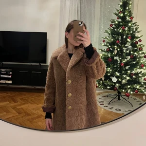 Brun teddyjacka med knappar - Mysig brun teddyjacka med stora knappar och bred krage. Perfekt för kyliga dagar med sin fluffiga och varma design. Jackan har långa ärmar och en avslappnad passform.