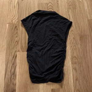 Mörk grå topp från Gina Tricot har använts få gånger i storlek xxs  - Mörkgrå topp från Gina Tricot i en enkel och stilren design. Toppen har en asymmetrisk passform med rynkade detaljer på sidan som ger en fin silhuett. 