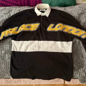 rugby shirt/piké från Palace - Snygg svart och vit pikétröja från Palace med texten 'Palace London' i gult och vitt över bröstet. Tröjan har en klassisk krage och knappar framtill. Underbar fit & kvalitet, älskar denna men får för lite användning hos mig.