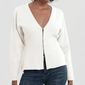 Vit kofta - Säljer en stilren vit ribbad kofta med v-ringning och knappar framtill. Koftan är croppad och har långa ärmar, perfekt för en trendig look. Tyvärr för stor för mig som vanligtvis har xxs