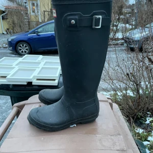 Svarta stövlar från Hunter - Säljer ett par klassiska svarta stövlar från Hunter. De är höga med en justerbar rem och spänne upptill. Perfekta för regniga dagar och leriga promenader.