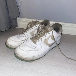 Vita Nike Air Force sneakers - Säljer ett par klassiska vita Nike Air Force sneakers med snörning. Skorna har en robust sula och den ikoniska Nike-loggan på sidan. Perfekta för en avslappnad stil. Det är inte så bra kvalite men man kan enkelt fräscha upp dom!