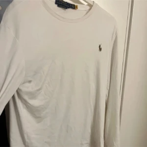 Vit långärmad tröja från Ralph Lauren - Säljer en klassisk vit långärmad tröja från Ralph Lauren med det ikoniska logotypbroderiet på bröstet. Perfekt för en stilren och avslappnad look.