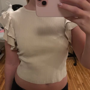 Beige ribbad topp med volangärmar - Säljer en söt beige ribbad topp med volangdetaljer på ärmarna. Toppen är croppad och har en rund halsringning. Väldigt sparsamt använd så i superbra skick🤍💛