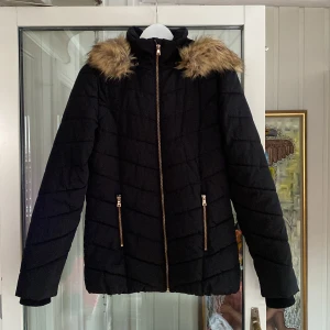Svart quiltad jacka med pälsdetaljer från KappAhl - Snygg svart quiltad jacka från KappAhl med dragkedja och huva. Jackan har pälsdetaljer runt huvan som är avtagbara och praktiska fickor med dragkedjor. Perfekt för kyliga dagar. Jackan är i storlek 170 men passar den som vanligtvis bär S. Jag kan mötas i city eller Västerort. Om man vill få varan hemskickad kostar frakten ca 118kr alltså 218kr totalt.