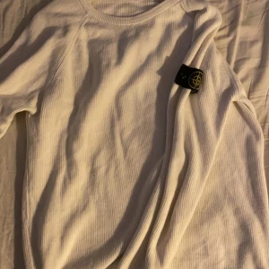 Vit ribbad tröja från Stone Island - Säljer en stilren vit ribbad tröja från Stone Island. Tröjan har en klassisk design med långärmade ärmar och en rund halsringning. Perfekt för en avslappnad och trendig look.