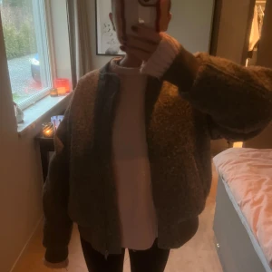 Grå bomberjacka - Säljer en snygg grå bomberjacka med dragkedja. Jackan har en mjuk och fluffig yta, perfekt för kyligare dagar. Den har en klassisk bomberstil med ribbade muddar vid ärmslut och krage.