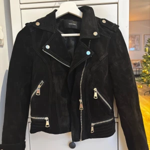 Svart mockajacka från Vero Moda - Snygg svart mockajacka från Vero Moda med dragkedjor och knappar. Jackan har en klassisk bikerstil med asymmetrisk dragkedja och flera fickor. Använts max 2 gånger på 1 år.