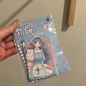 Blue Angel sticker - Ett set med 10 kort med motiv av en tecknad figur i blå klänning och långt hår. Förpackningen har en blå bakgrund med rutmönster och texten 'Blue Angel'. Perfekt för samlare eller som dekoration.