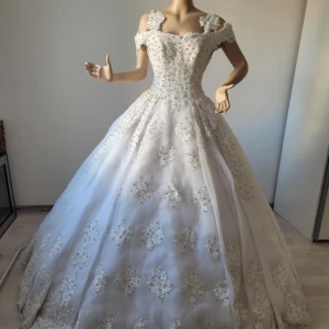 Vit brudklänning med spetsdetaljer - Elegant vit brudklänning med offshoulder-design och vackra spetsdetaljer. Klänningen har en klassisk lång siluett och är perfekt för en sagolik bröllopsdag. 