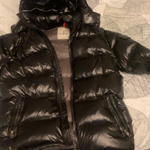 Svart dunjacka från Moncler - Snygg svart dunjacka från Moncler med glansig finish och huva. Jackan har dragkedja framtill och praktiska fickor med dragkedjor. Perfekt för kyliga dagar med stil.Har inte använt den länge köptes föra vintras. (Kom dm om du är intresserad)