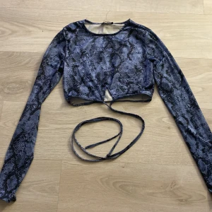 Blå ormmönstrad croppad topp från Tally Weijl - Snygg blå croppad topp med ormmönster från Tally Weijl. Toppen har långa ärmar och en knytning i midjan för en trendig look. Perfekt för att sticka ut i mängden!