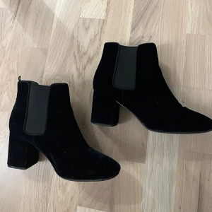 Svarta Chelsea boots H&M - Snygga marinblå Chelsea boots med klack i sammet. De har en klassisk design med elastiska paneler på sidorna för enkel på- och avtagning. Perfekta för både vardag och mer uppklädda tillfällen.