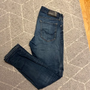 Blå jeans från Jack & Jones - Snygga blå jeans från Jack & Jones i modellen Slim/Glenn. De har en klassisk femficksdesign och en bekväm passform. Perfekta för en stilren look. Storlek 32/32 dem har slitningar vid knäna