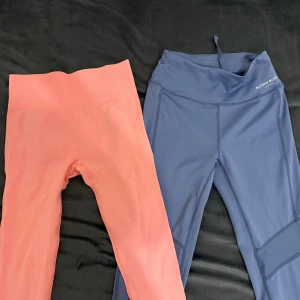 Två par träningstights - Säljer två par träningstights. Ett par i korallrosa och ett par i marinblått. Båda har hög midja och är tillverkade i ett stretchigt syntetmaterial. Perfekta för gymmet eller yoga.