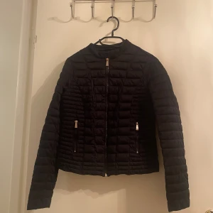 Svart pufferjacka från Amisu - Snygg svart pufferjacka från Amisu med dragkedja framtill och två fickor med dragkedjor. Jackan har en stilren design och är perfekt för kyligare dagar.