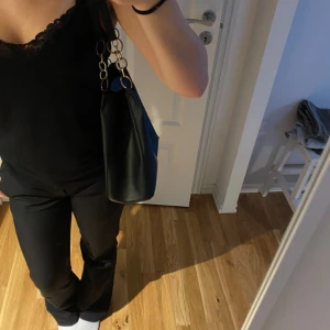 Svart axelväska  - Väskan är i bra skick men använd, den är helt svart med guld kedja, rymmer mycket,  Längd: 29,5 cm Bredd: 11,5 cm Höjd: 25,5 cm 