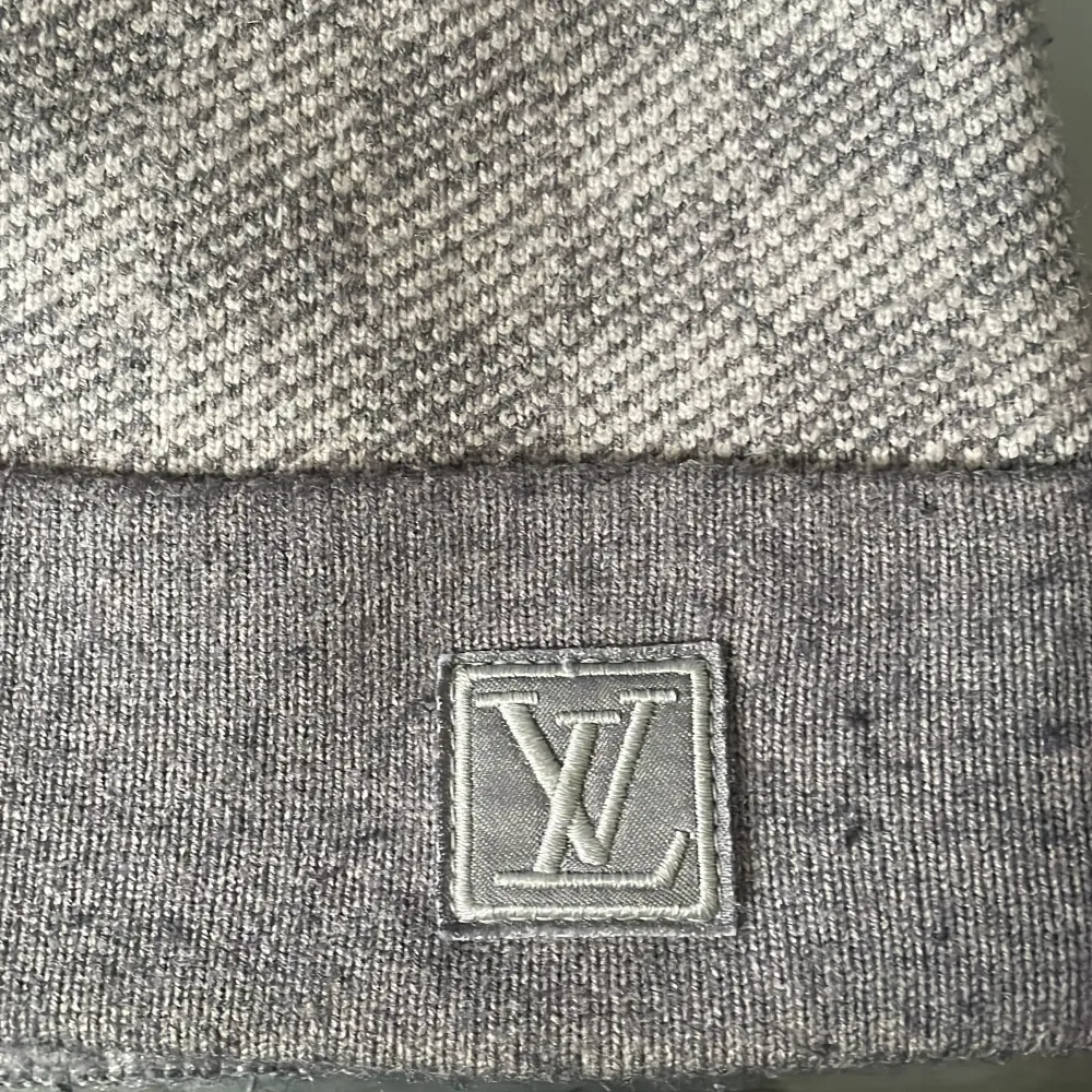 Säljer en stilren och lyxig grå mössa från Louis Vuitton. Den har ett diskret rutigt mönster och är prydd med LV-loggan på uppviket. Perfekt för att hålla sig varm med stil under kyliga dagar.. Accessoarer.