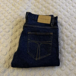 Mörkblå jeans från Tiger of Sweden - Snygga mörkblå jeans från Tiger of Sweden med klassisk femficksdesign och gul kontrastsöm. Perfekta för en stilren look. Märkeslapp i läder baktill ger en exklusiv touch. 🔴Nypris: 1200 kr, 🟢Mitt pris: 500 kr. Endast använda ett fåtal gånger, utan synliga defekter. Skriv vid minsta fundering.