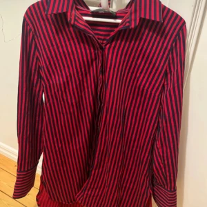 Röd och svart randig skjorta från By Malene Birger - .Snygg röd och svart randig skjorta från By Malene Birger. Skjortan har långa ärmar och klassisk krage, perfekt för en stilren look. Tillverkad i en bomullsblandning för en bekväm passform. Liten i storleken så skulle säga att den passar M/38. Säljer en likadan i storlek M/38 och passar precis som en M/38.