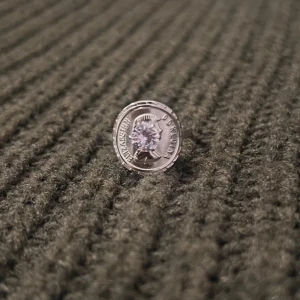 Roman Empire Legacy - Silver Ring with Coin & Stone - US storlek 8,5, diameter 18,1 mm, omkrets 56,8 mm. Denna ring kombinerar historisk charm med modern design, där en sten sitter på ett mynt inspirerat av det romerska imperiet. Den justerbara passformen säkerställer både komfort och stil.