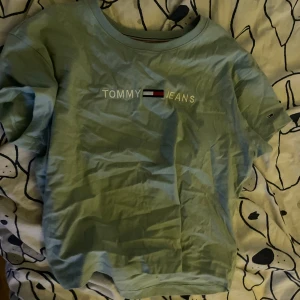Ljusblå t-shirt från Tommy Jeans - Säljer en ljusblå t-shirt från Tommy Jeans med deras ikoniska logga på bröstet. T-shirten har korta ärmar och en rund halsringning. Perfekt för en avslappnad stil.