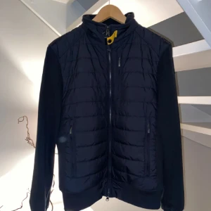 Svart pufferjacka från Parajumpers - Hej, säljer nu min parajumper cardigan som inte har använts mer än 3gånger. Detta berodde på att jag inte blev nöjd med storleken. Finns en qr kod så ni kan kontrollera att den är äkta, den är också köpt på Urban model på väla i Helsingborg👍🏼bara att skriva ifall ni har frågor😁ordinarie pris 4000kr
