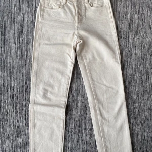 Beige byxor från Dagmar - Snygga beige byxor från Dagmar i ekologisk bomull med en liten del elastan för extra komfort. De har en klassisk design med knapp och dragkedja framtill. Perfekta för en stilren look. Nya naturvita jeans i strl 34 från House of Dagmar.  Nya, aldrig använda.  Mått Midjan: ca 36 cm Längd från grenen och ner: ca 69 cm  99% ekologisk bomull och 1% elastan  Kommer från ett djur och rökfritt hem.