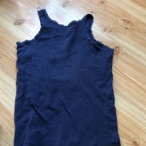 Mörkblå linnetopp från OVS - Säljer en mörkblå linnetopp från OVS med spetsdetaljer runt halsringningen och ärmhålen. Perfekt för varma dagar eller som ett lager under andra plagg. Enkel och stilren design som passar till mycket.