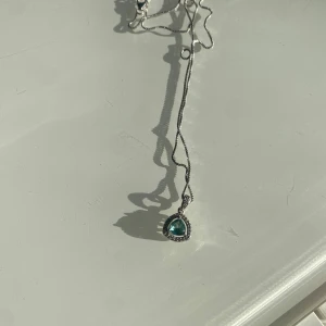 Halsband med turkos sten - Elegant halsband med en triangulär turkos sten infattad i en silverfärgad ram. Kedjan är tunn och justerbar