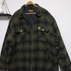 Grönrutig jacka med dragkedja - Säljer en grönrutig jacka med dragkedja och krage. Jackan har två bröstfickor med knappar och en quiltad insida för extra värme. Perfekt för kyligare dagar.