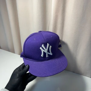 New Era keps - Snygg lila keps från New Era med broderad vit logga framtill. Kepsen har en rak skärm och är i modellen 59FIFTY. Perfekt för att ge din outfit en färgklick!