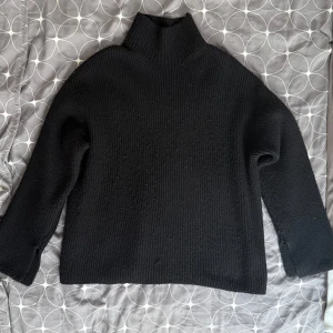 Svart stickad polotröja - Säljer en stilren svart stickad polotröja med hög krage. Tröjan har långa ärmar och en lös passform med diskret slitt i vardera ärm. Passar bra till både jeans och kjol. Org pris 250kr        Strlk L men passar S