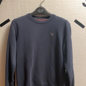 Mörkblå tröja från Gant - Säljer en stilren mörkblå tröja från Gant med rund halsringning och diskret logotyp på bröstet. Inga defekter förutom lite solblekt. Passar 164-170 men passar xs-s. Pris kan diskuteras