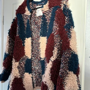 Flerfärgad teddyjacka från Pull&Bear - Säljer en mysig och trendig teddyjacka från Pull&Bear i storlek M. Jackan har ett unikt flerfärgat mönster i vinrött, beige och blått. Perfekt för att hålla sig varm och stilren under kyliga dagar.