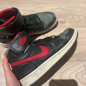 Nike Air Jordans i svart och rött - Säljer ett par klassiska Nike Air Jordans i svart och rött. Skorna har en röd Nike-logga på sidan och svart snörning. De är tillverkade i skinn och har en robust sula för bra grepp. Perfekta för dig som älskar sneakers med stil.