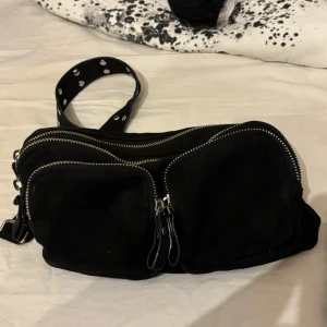 Svart axelväska från Gina Tricot - Snygg svart axelväska från Gina Tricot med flera dragkedjefickor för praktisk förvaring. Perfekt för att bära dina dagliga nödvändigheter med stil.