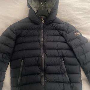 Mörkblå dunjacka från Colmar - Säljer en snygg mörkblå dunjacka från Colmar med huva och dragkedja. Jackan har en quiltad design och praktiska fickor med dragkedjor. Perfekt för kyliga dagar.