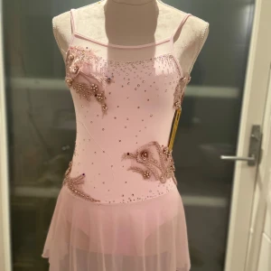 Rosa konståkningsklänning - Elegant rosa klänning med tunna axelband och vackra pärldetaljer. Klänningen har en mjuk, flödande kjol och är dekorerad med blommiga broderier och detaljerad med stenar// jag har blingat och håller nu på att sy fast blomdetaljerna, den är långt ifrån klar men vid intresse säg till då jag ska försöka hinna klart med den( ifall man önskar något extra på klänningen är det bara att säga till)