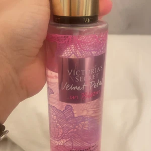 Victoria's Secret Velvet Petals in Bloom - En doftspray från Victoria's Secret med namnet Velvet Petals in Bloom. Flaskan är dekorerad med rosa blommönster och har en gyllene kork. Perfekt för den som älskar blommiga och fräscha dofter.