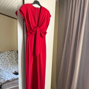 Röd jumpsuit  från Mango - Snygg röd jumpsuit från Mango med en elegant knytdetalj framtill. Klänningen har en dragkedja i ryggen och är ärmlös, vilket ger en stilren look. Perfekt för speciella tillfällen när du vill sticka ut. 💃
