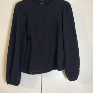 Svart långärmad topp från VeroModa - Säljer en stilren svart topp från VeroModa med långa puffiga armar och en texturerad yta. Perfekt för en elegant look. Toppen har en rund halsringning och är tillverkad i ett bekvämt material. Den använd fåtal gånger😊