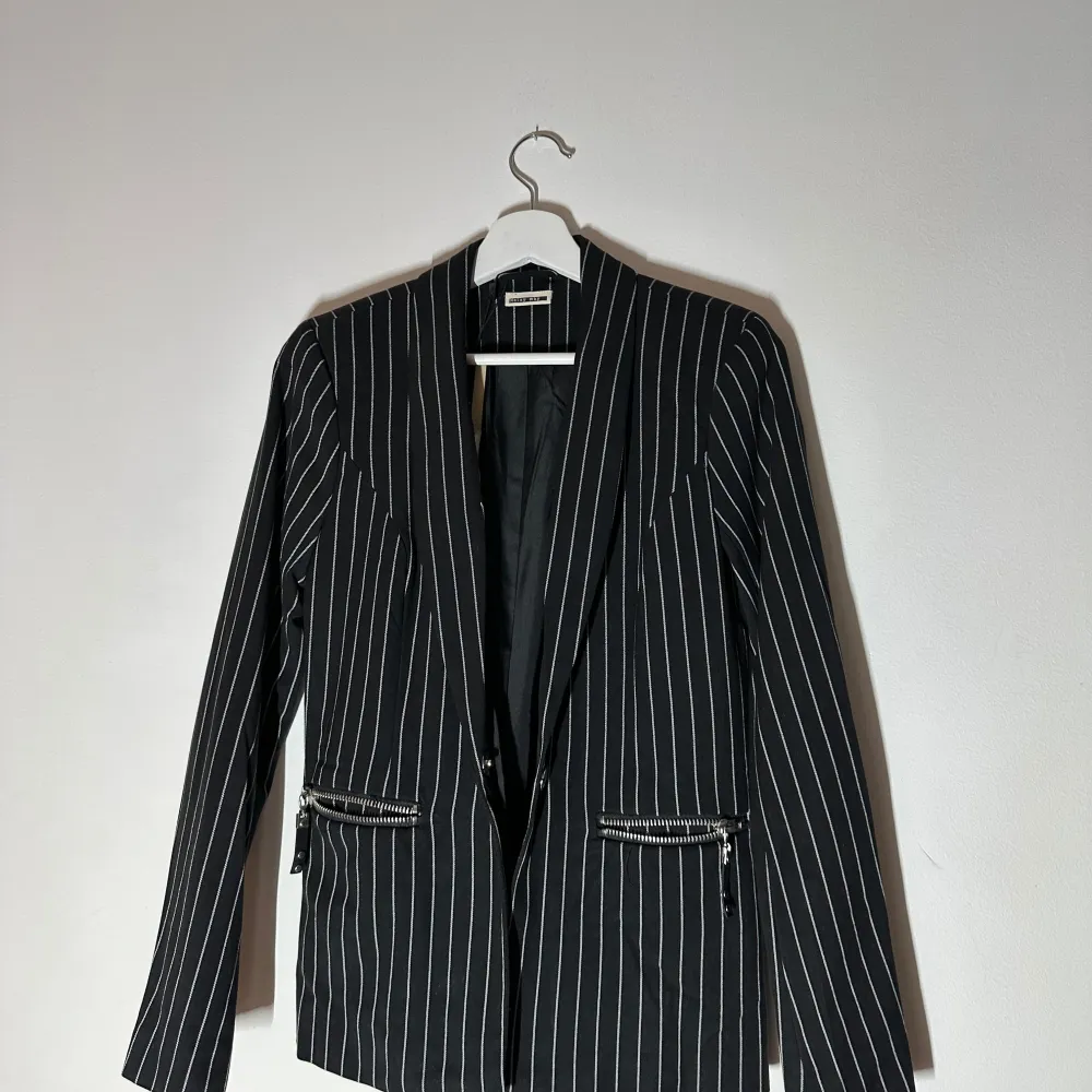 Snygg svart kavaj med vita ränder från Rosy Boy. Kavajen har en klassisk passform med dragkedjor vid fickorna för en modern touch. Perfekt för att ge en stilren look till din outfit.🥰🥰🥰. Puvut & Bleiserit.