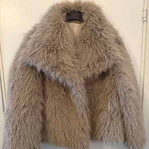Beige pälsjacka - Säljer en fluffig och trendig beige pälsjacka med stor krage. Jackan har en oversized passform och är perfekt för kyliga dagar. Den är långärmad och ger en lyxig känsla. Perfekt för att göra ett statement i vintergarderoben.