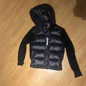 Sixties cardigan - Säljer en svart pufferjacka från G-Star med avtagbar huva och dragkedja. Jackan har långa ärmar i stickat material och en quiltad design. Perfekt för kyliga dagar!