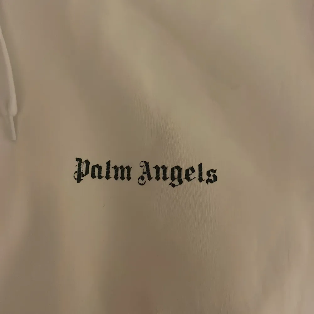 Säljer en stilren vit hoodie från Palm Angels med deras ikoniska logga tryckt både fram och bak. Hoodien har en klassisk passform med långa ärmar och en praktisk ficka framtill. Perfekt för en avslappnad look.färgen bak har släppt lite men inte mätbart alltså på texten . Neuletakit & Villapaidat.
