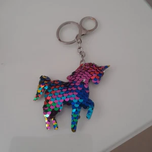 Nyckelring med enhörning i paljetter - Färgglad nyckelring formad som en enhörning, täckt med skimrande paljetter i regnbågens alla färger. Perfekt accessoar för att lysa upp dina nycklar eller väskor.