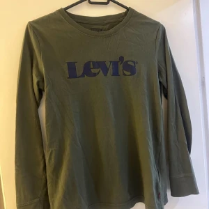 Grön långärmad tröja från Levi's - Säljer en grön långärmad tröja från Levi's med tryckt logotyp på bröstet. Perfekt för en avslappnad stil. Tröjan är tillverkad i mjukt material och har en rund halsringning.